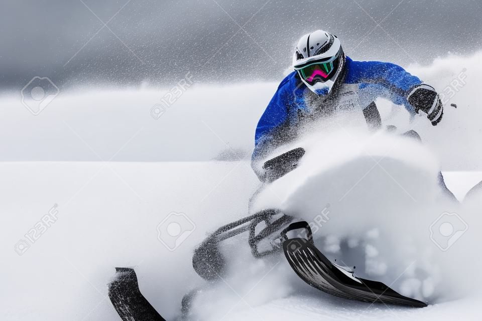 In deep snowdrift snowmobile rider driving fast. Riding with fun in white snow powder during backcountry tour. Extreme sport adventure, outdoor activity during winter holiday on ski mountain resort.