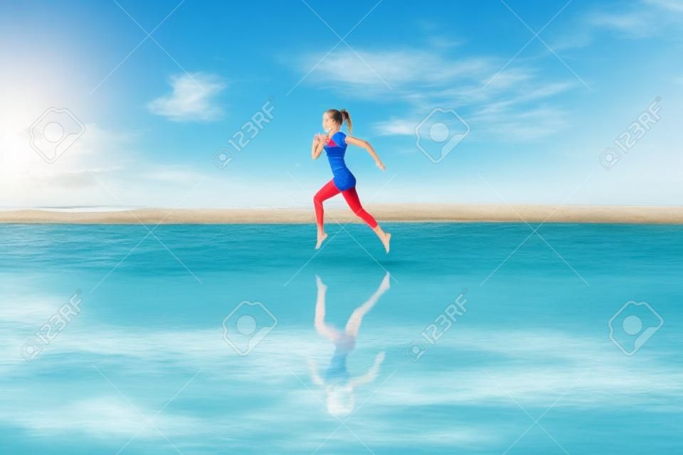 Boso młoda dziewczyna z szczupłą sylwetką biegnącą wzdłuż morza przy basenie z wodą, aby zadbać o kondycję i spalać tłuszcz. plaża tło z błękitnym niebem. kobieta fitness, jogging aktywności sportowej na letnie rodzinne wakacje.