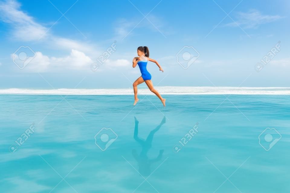 Boso młoda dziewczyna z szczupłą sylwetką biegnącą wzdłuż morza przy basenie z wodą, aby zadbać o kondycję i spalać tłuszcz. plaża tło z błękitnym niebem. kobieta fitness, jogging aktywności sportowej na letnie rodzinne wakacje.