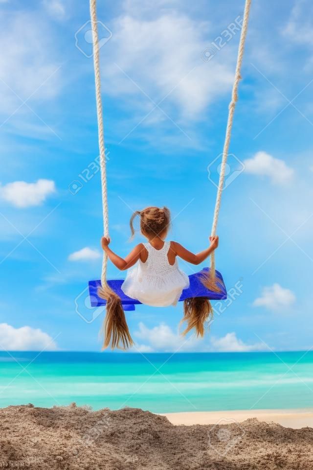 Szczęśliwa dziewczyna dobrze się bawi kołysząc się wysoko w powietrzu. latanie do góry nogami na huśtawce liny na plaży. podróż przygoda na rajskiej tropikalnej wyspie. rodzinny styl życia, aktywność na wakacjach z dziećmi