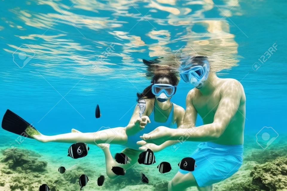 幸せな家族の休暇。シュノーケリングマスクの若いカップルが手をつないで、サンゴ礁の海のプールで魚と一緒に水中に飛び込みます。旅行のライフスタイル、ウォータースポーツの冒険、夏のビーチホリデーの水泳活動