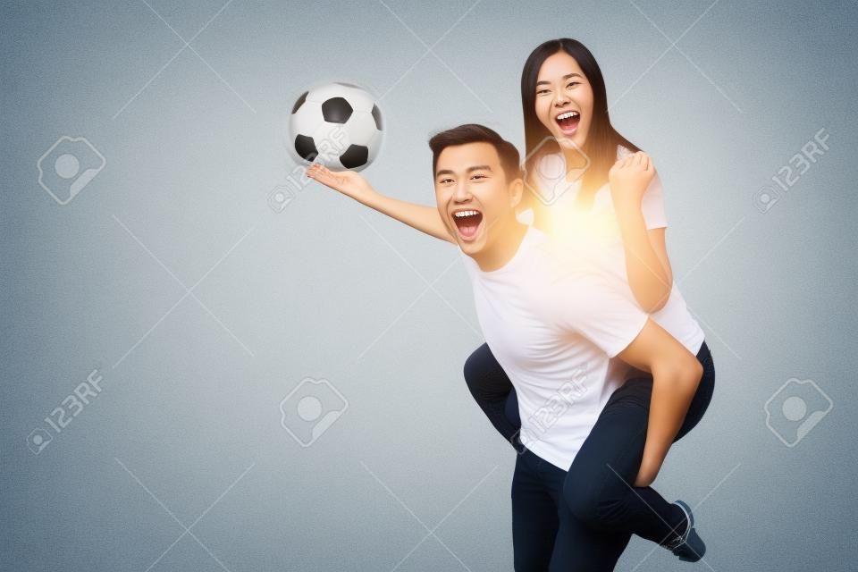 Inspired young couple, woman sit on man piggyback, fans with soccer ball cheering favorite football team expressive gesticulating hands isolated on white background. Family leisure, lifestyle concept