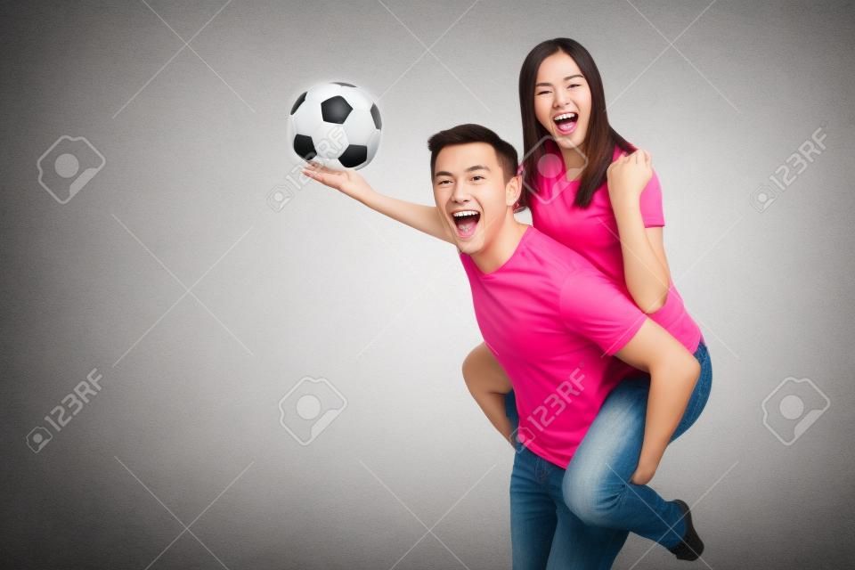 Inspired young couple, woman sit on man piggyback, fans with soccer ball cheering favorite football team expressive gesticulating hands isolated on white background. Family leisure, lifestyle concept