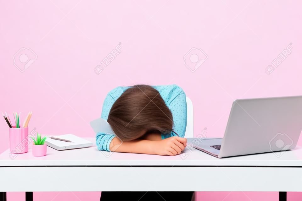 Young Disappointed Tired woman laid her head down on the table sit, work at white desk with contemporary pc laptop isolated on pastel pink background. Achievement business career concept. Copy space