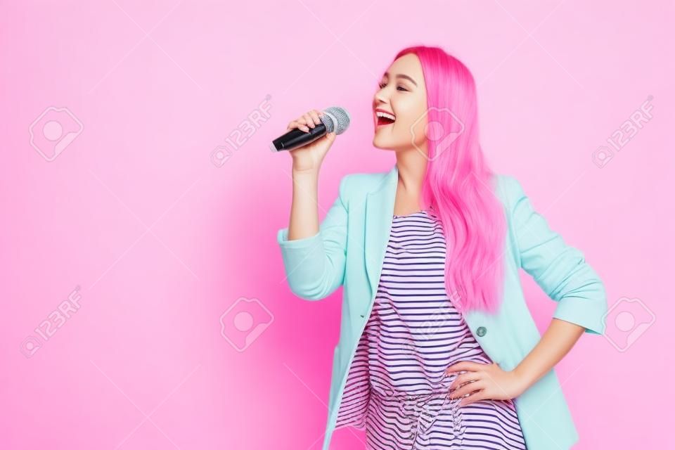 Porträt einer fröhlichen jungen Frau in gestreifter Jacke, die zur Seite schaut, singt ein Lied im Mikrofon, isoliert auf rosa Pastellhintergrund im Studio. Menschen aufrichtige Emotionen, Lifestyle-Konzept. Mock-up-Kopienbereich