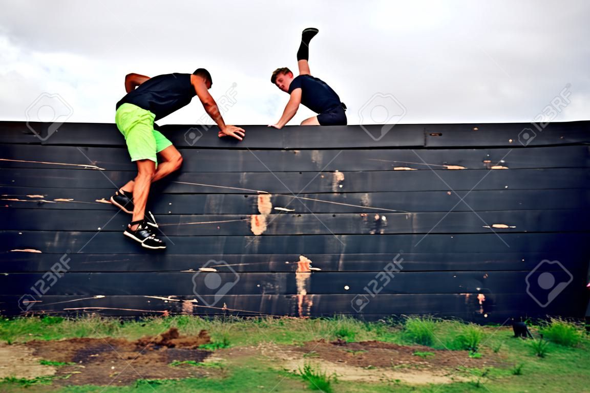 Two participants in an obstacle course climbing a wall