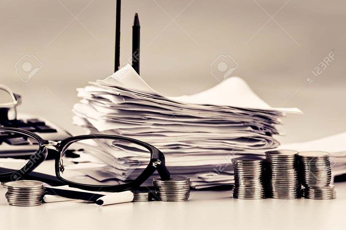 Receipts in paper nail with eyeglasses, pen and heap coins stair