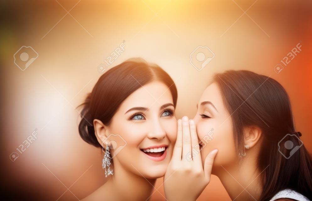la amistad, la felicidad y el concepto de la gente - dos mujeres sonrientes que susurran chisme