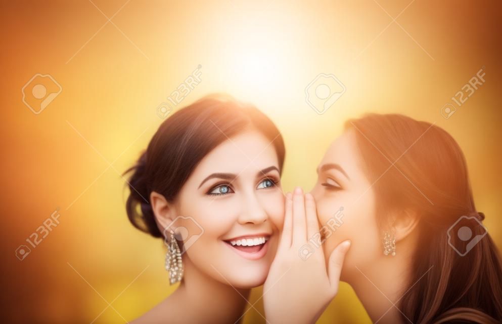 la amistad, la felicidad y el concepto de la gente - dos mujeres sonrientes que susurran chisme