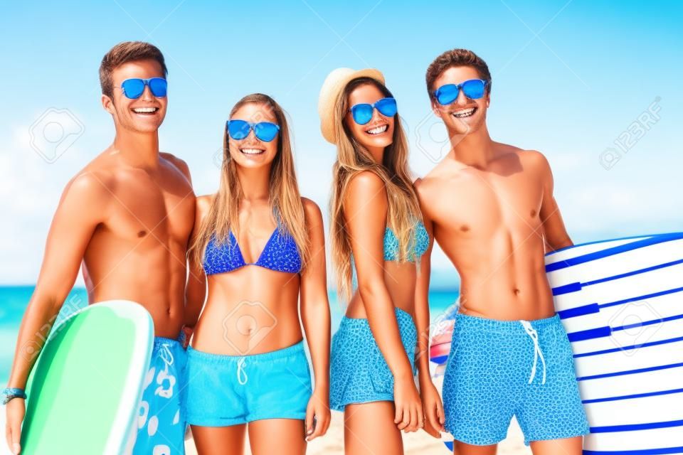 l'amitié, la mer, les vacances d'été, le sport et les gens de l'eau notion - groupe de sourire amis portant maillots de bain et lunettes de soleil avec des planches de surf sur la plage