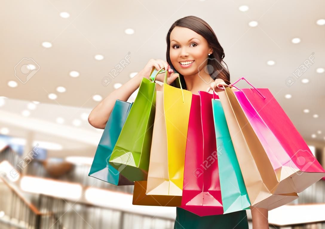 행복, 소비, 판매 및 사람들이 개념 - 쇼핑몰 배경 위에 쇼핑 가방과 함께 웃는 젊은 여자