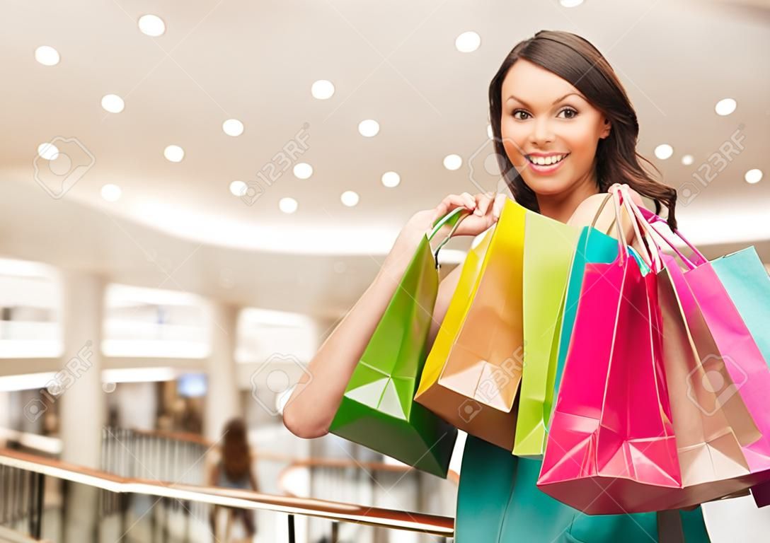 행복, 소비, 판매 및 사람들이 개념 - 쇼핑몰 배경 위에 쇼핑 가방과 함께 웃는 젊은 여자