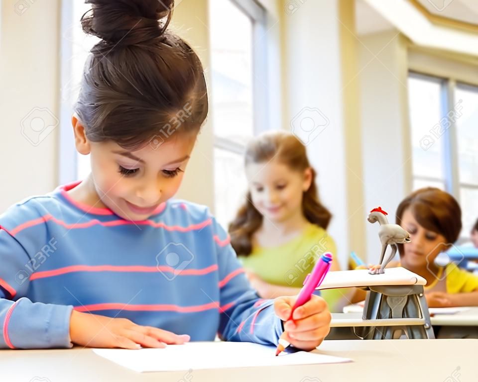 教育，小學和兒童的理念 - 快樂的小女孩的學生用紙筆寫了classrom和教師背景
