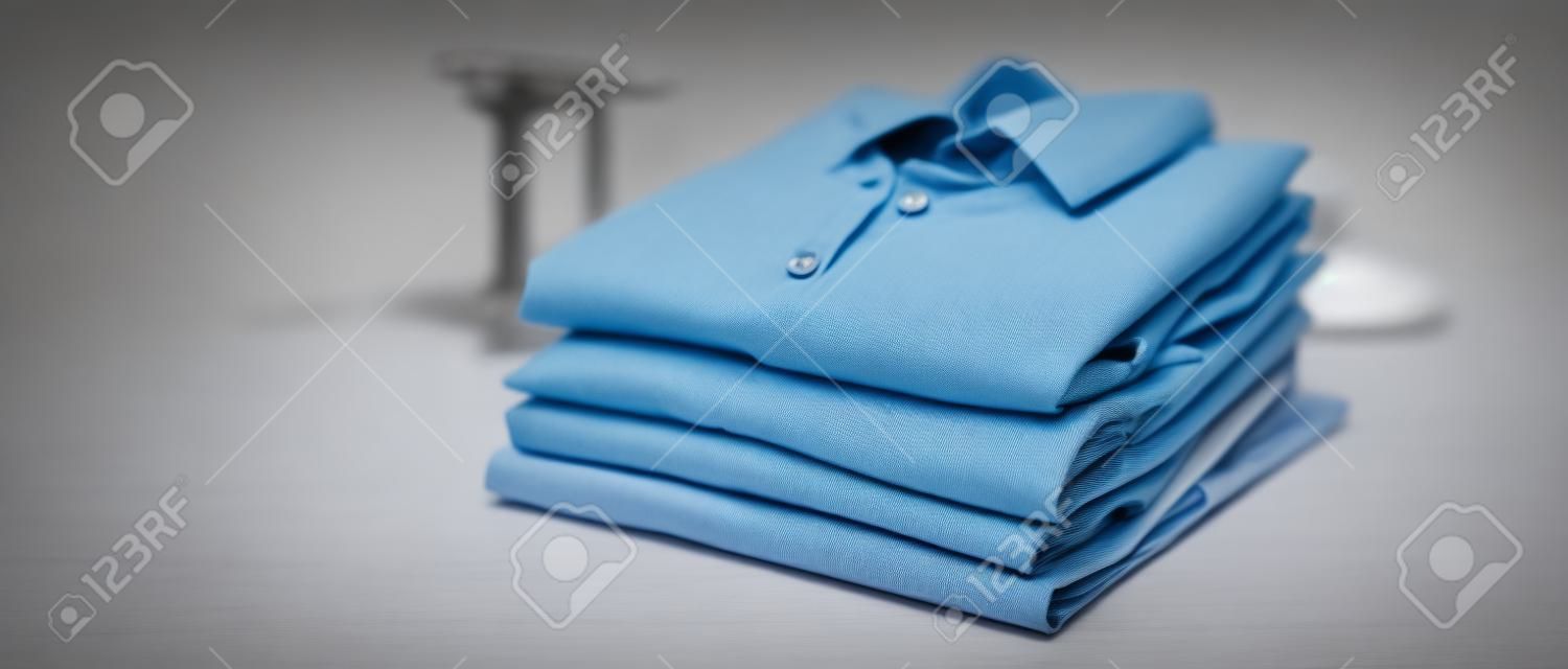熨烫、洗衣、衣服、家务和物品的概念--熨烫和折叠的衬衫放在家里的桌子上