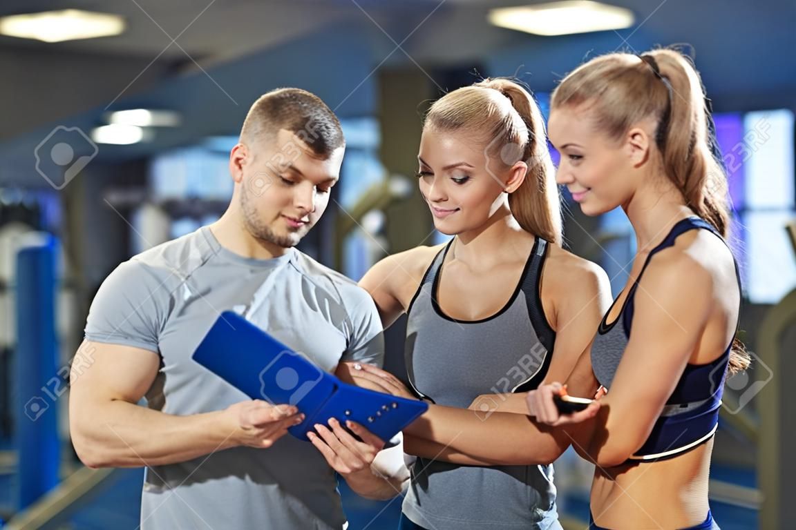 Fitness, spor, egzersiz ve diyet kavramı - panoya spor salonunda egzersiz planı yazma ile genç kadın ve kişisel antrenör gülümseyen