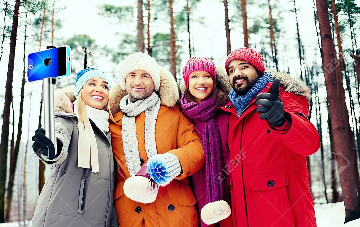 技術，季節，友誼和人的概念 - 一群微笑的男性和女性服用selfie與智能手機和腳架冬季森林