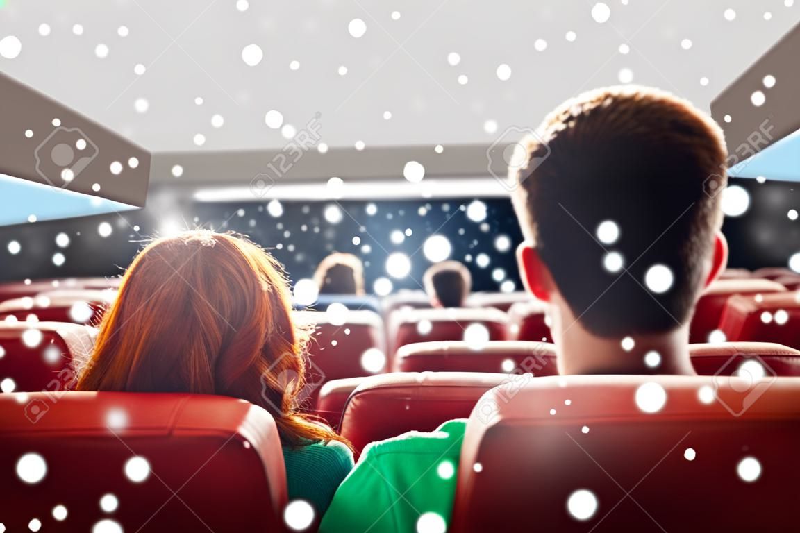 映画館、娯楽、レジャー、人々 コンセプト - 雪片を後ろから映画館で映画を見てカップル