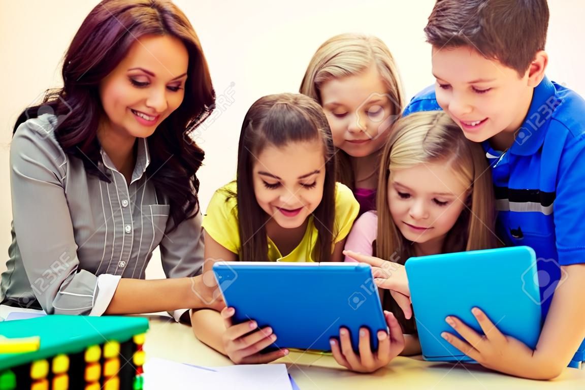 образование, начальная школа, обучение, технологии и люди концепции - группа школьников с учителем, глядя на компьютер планшетного компьютера в классе