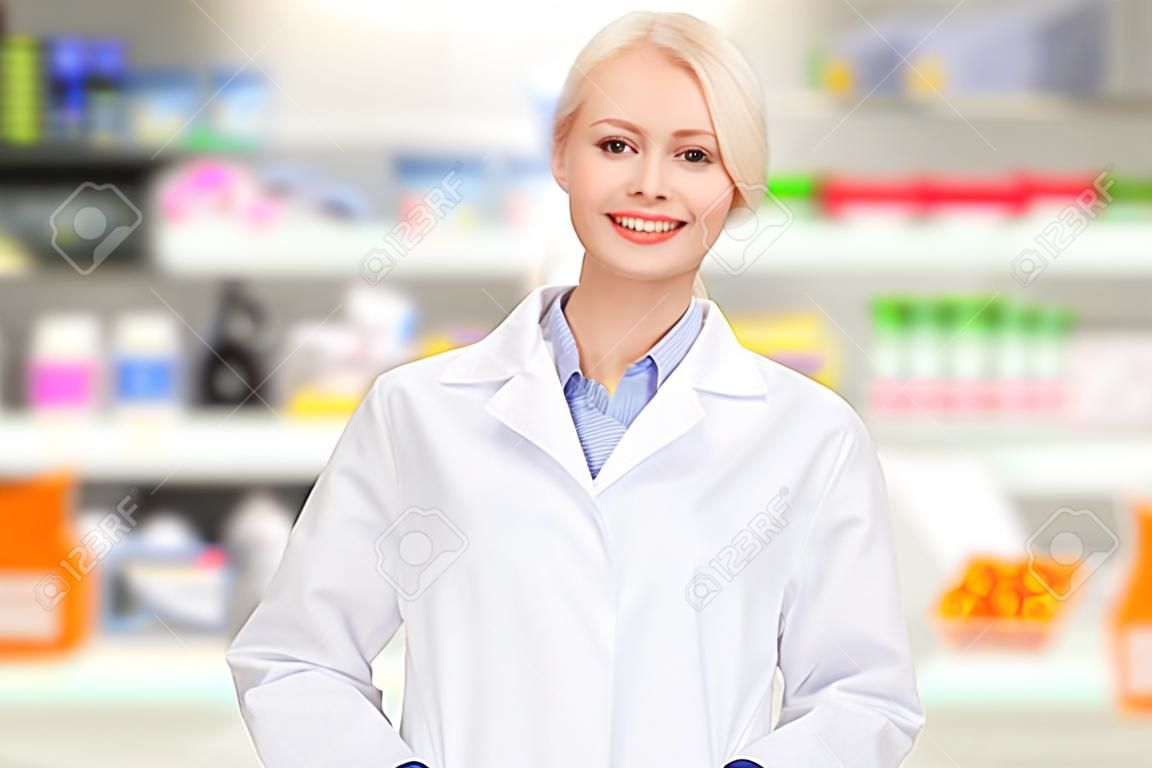 медицина, аптека, люди, здравоохранение и концепция фармакология - счастливая молодая женщина, фармацевт над аптечной фоне