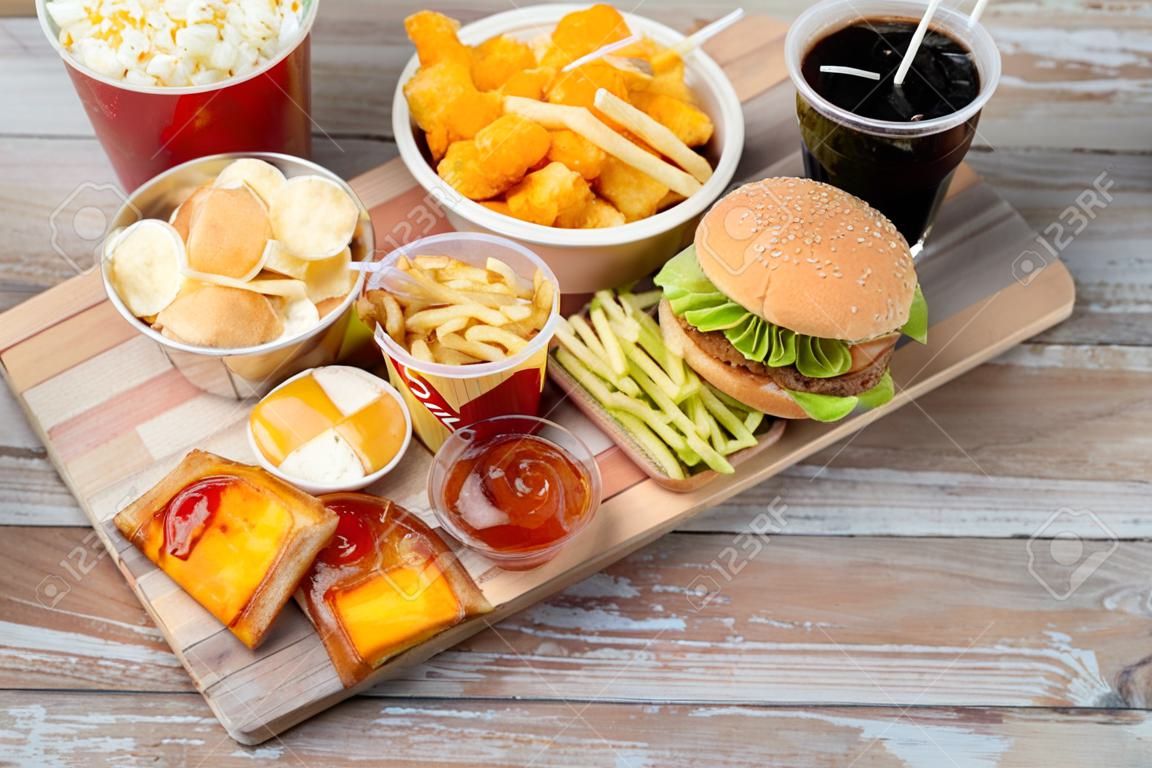fast food e conceito de alimentação pouco saudável - close up de lanches de fast food e bebida de coca cola na mesa de madeira