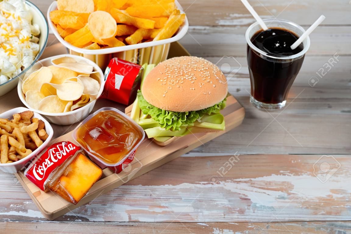 Fast Food und ungesunde Ernährung Konzept - Nahaufnahme von Fast-Food-Snacks und Coca Cola-Getränk auf Holztisch