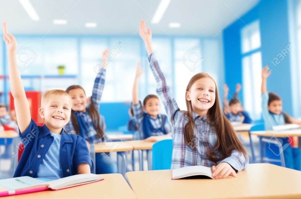l'éducation, l'école primaire, l'apprentissage et les gens concept - groupe d'enfants de l'école avec les ordinateurs portables assis dans la classe et à main levée
