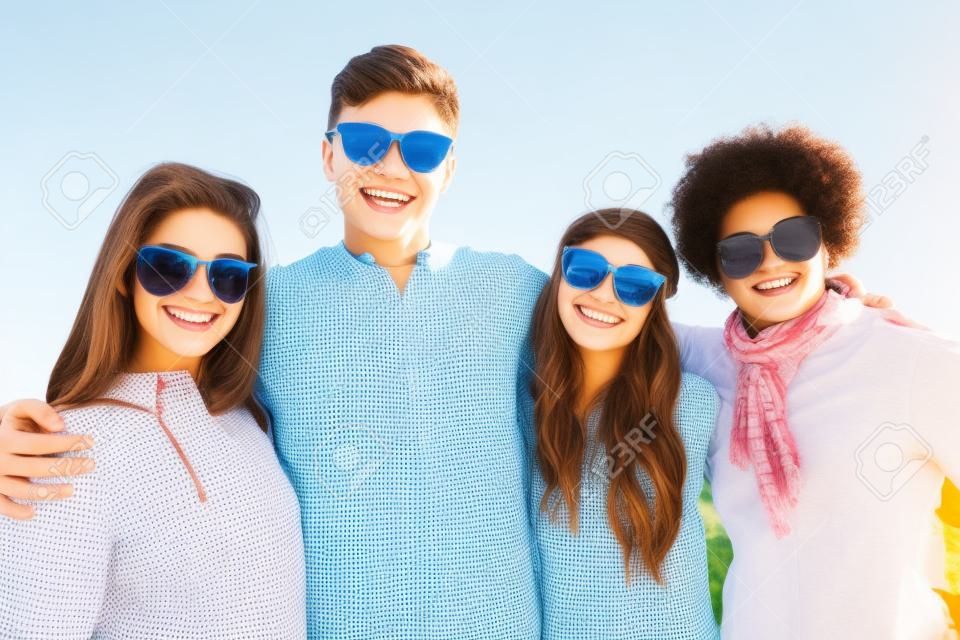 Freundschafts-, Tourismus-, Reise- und Leutekonzept - Gruppe glückliche Jugendfreunde in der Sonnenbrille, die draußen umarmt