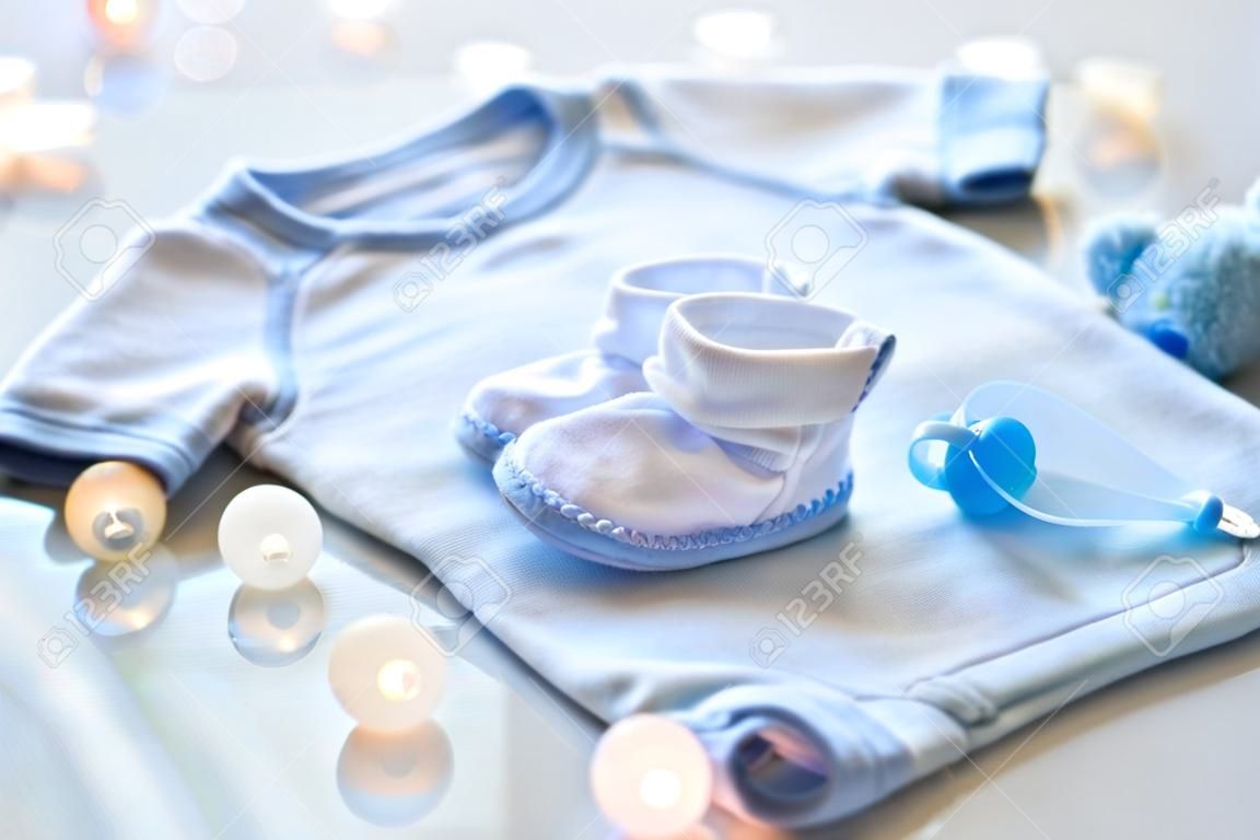 baby clothes, babyhood, motherhood and object concept - close up of white bodysuit, bootees and soother for newborn boy on table