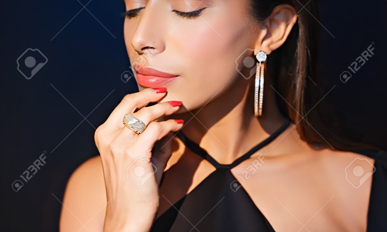 la gente, di lusso, gioielli e concetto di moda - bella donna in nero indossando orecchini di diamanti e l'anello su sfondo scuro