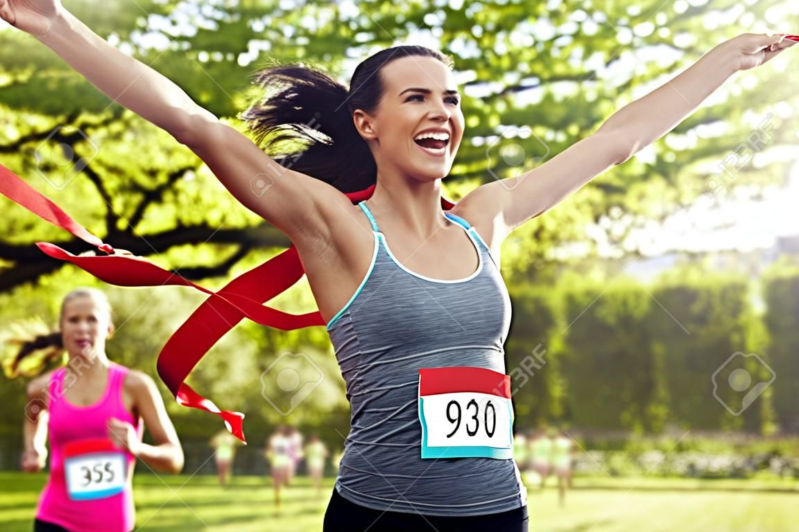 fitness, esporte, vitória, sucesso e conceito de estilo de vida saudável - corrida vencedora de mulher feliz e primeiro a terminar a fita vermelha sobre o grupo de desportistas correndo maratona com números de distintivo ao ar livre