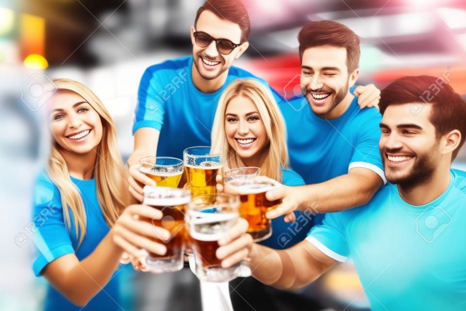 koncepcja sportu, piłki nożnej, ludzi i wypoczynku - szczęśliwi przyjaciele lub fani piłki nożnej stukający szklankami piwa i świętujący zwycięstwo w barze lub pubie