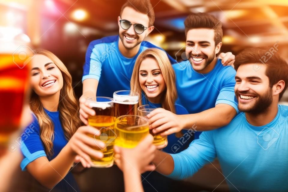 koncepcja sportu, piłki nożnej, ludzi i wypoczynku - szczęśliwi przyjaciele lub fani piłki nożnej stukający szklankami piwa i świętujący zwycięstwo w barze lub pubie