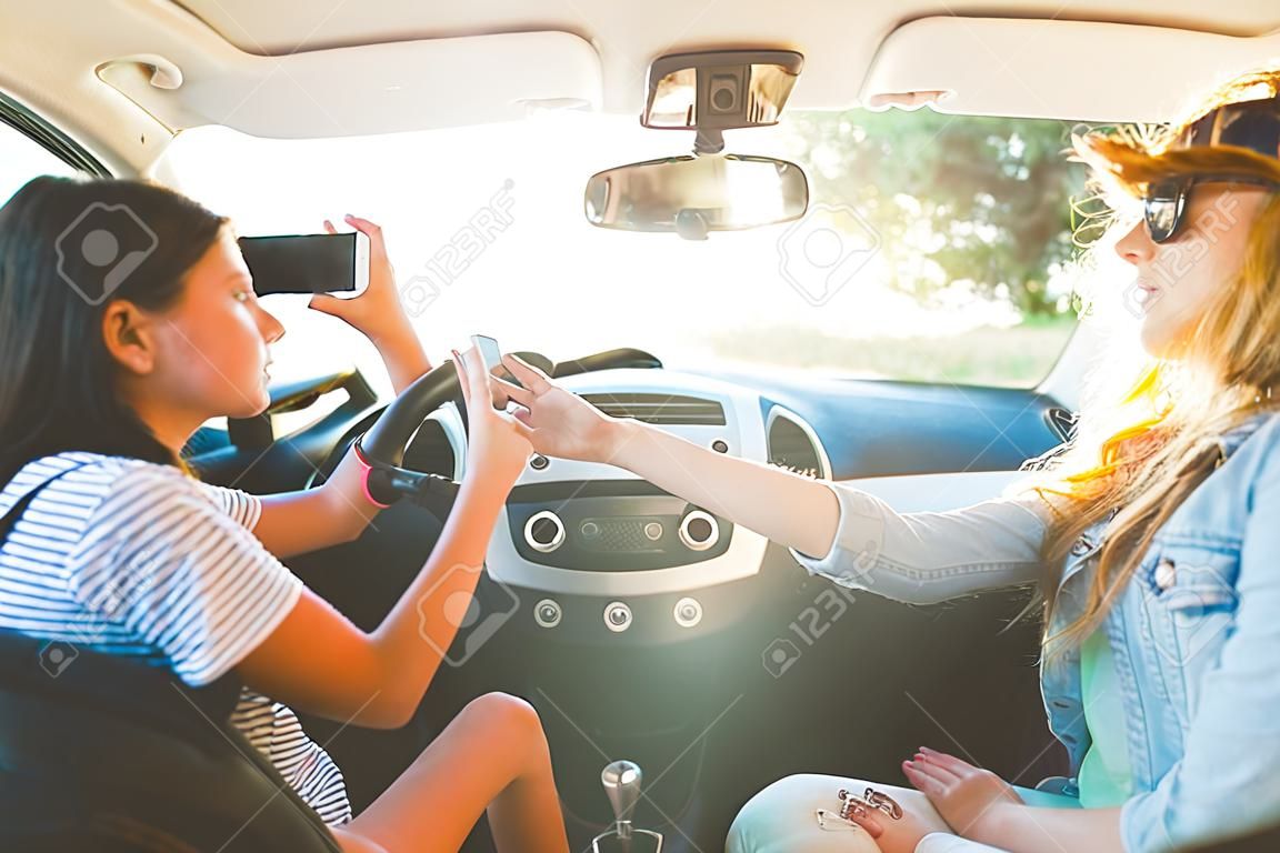 summer vacation, holidays, travel, road trip and people concept - happy teenage girls or young women with smartphone taking selfie in car