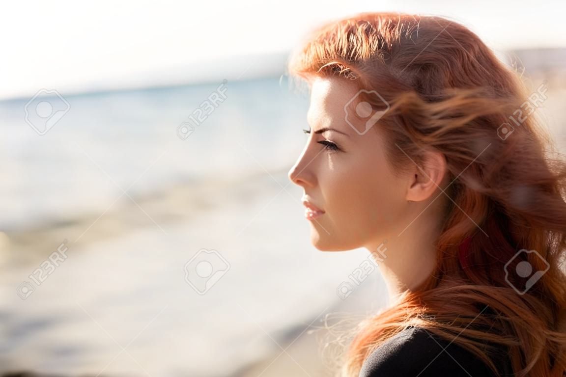 люди, выражение лица и концепция эмоция - счастливая молодая рыжеволосая женщина лицо на пляже