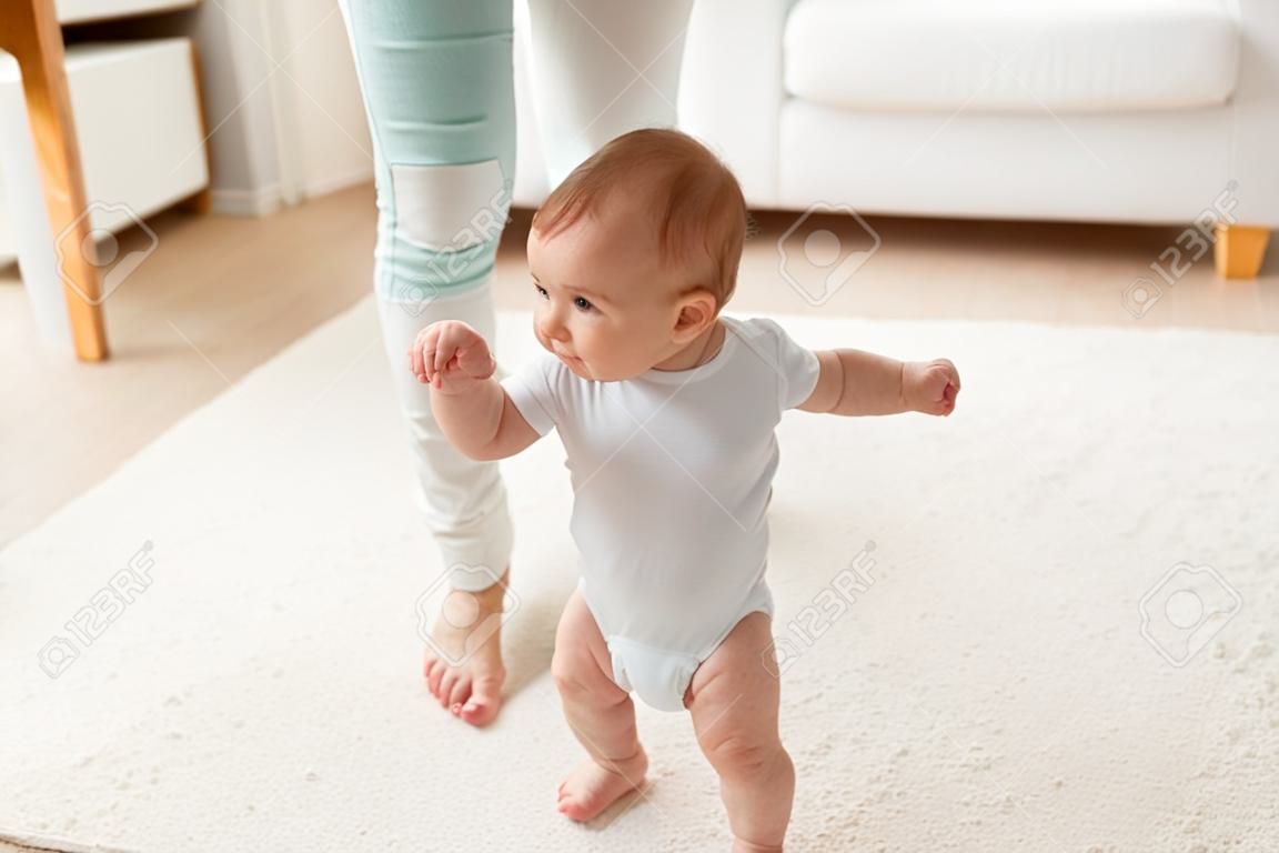 family, child, childhood and parenthood concept - happy little baby learning to walk with mother help at home