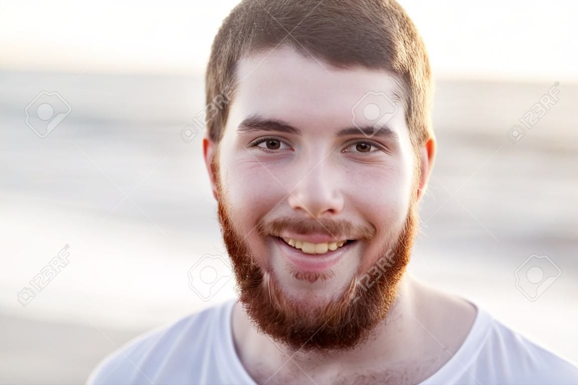 la gente, la emoción y el concepto de expresión facial - cara de feliz sonriente joven con barba roja en la playa