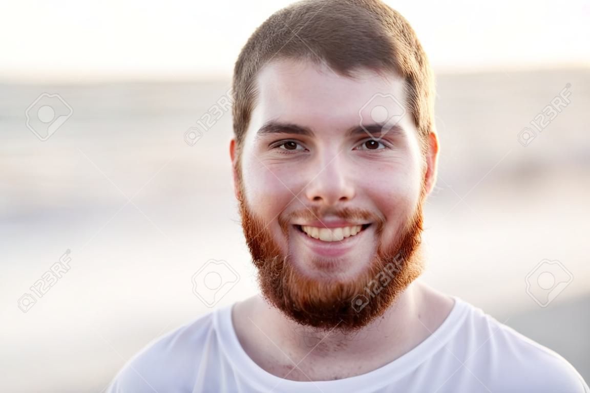 persone, emozione e il concetto espressione facciale - volto di giovane uomo sorridente con la barba rossa sulla spiaggia