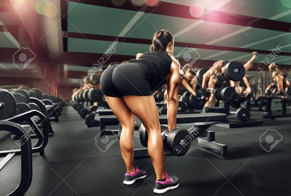 Mujer joven flexionando los músculos con pesas en el gimnasio