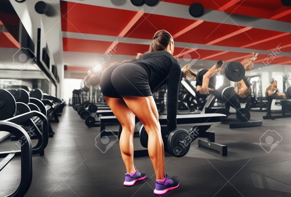 Mujer joven flexionando los músculos con pesas en el gimnasio