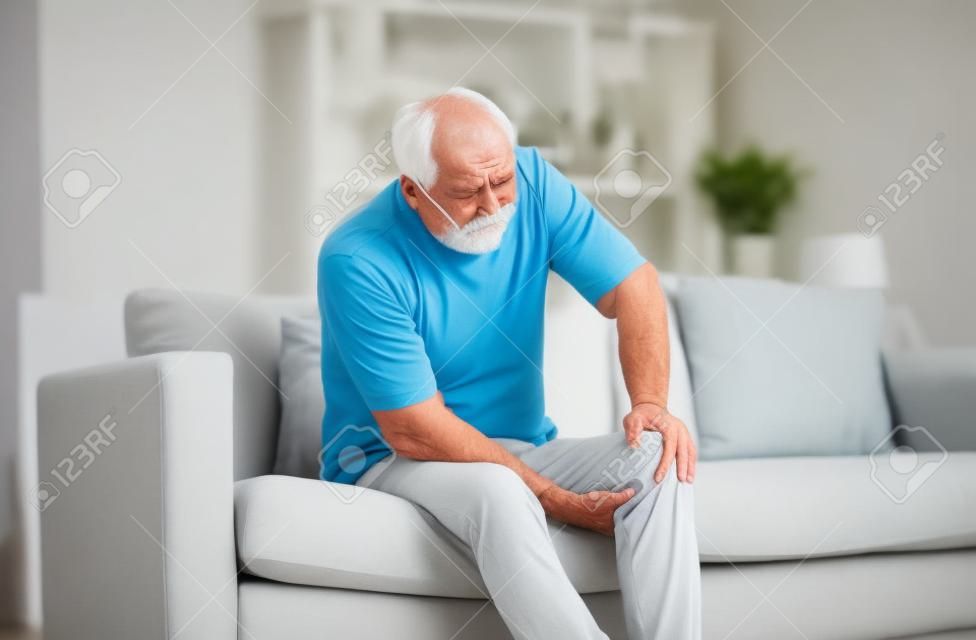 senior man suffering from knee ache at home