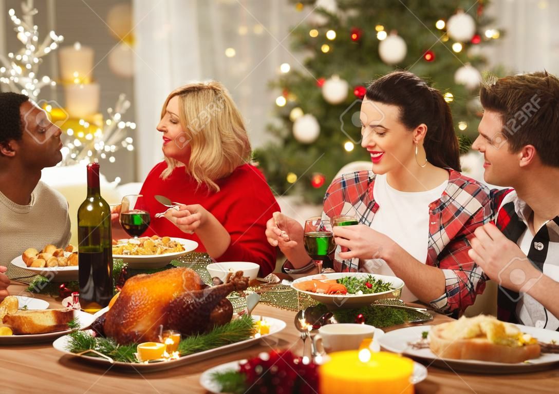 holidays and celebration concept - happy friends having christmas dinner at home and eating food