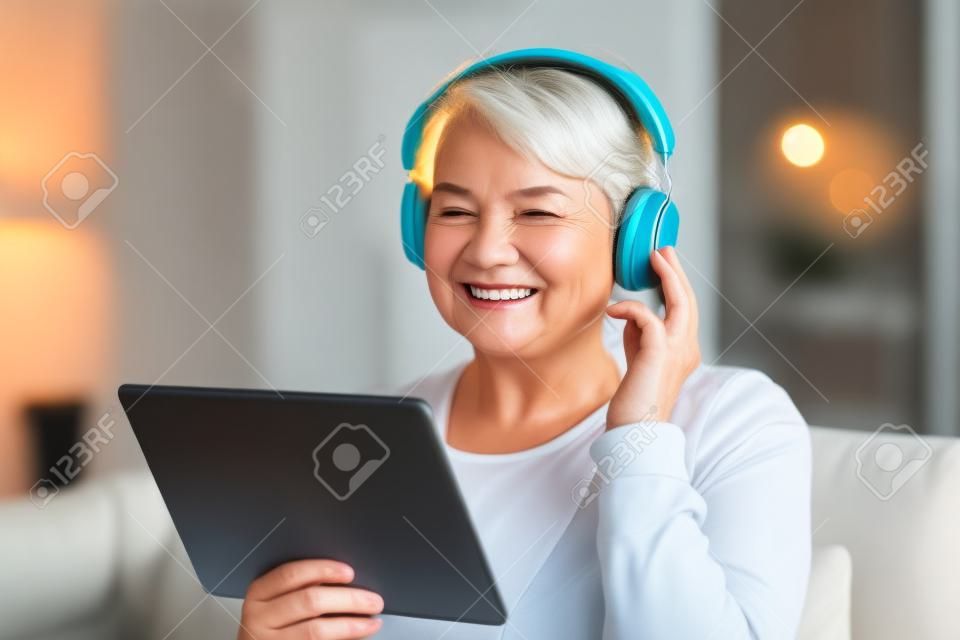 technology, people and lifestyle concept - happy senior woman in headphones and tablet pc computer listening to music at home in evening