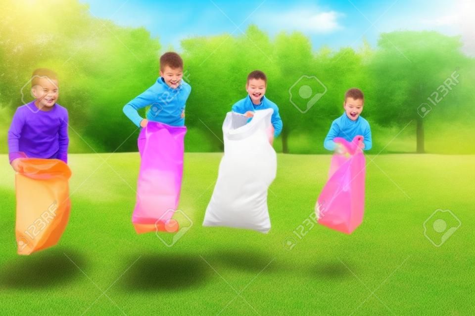 crianças felizes que jogam o jogo do salto do saco no parque