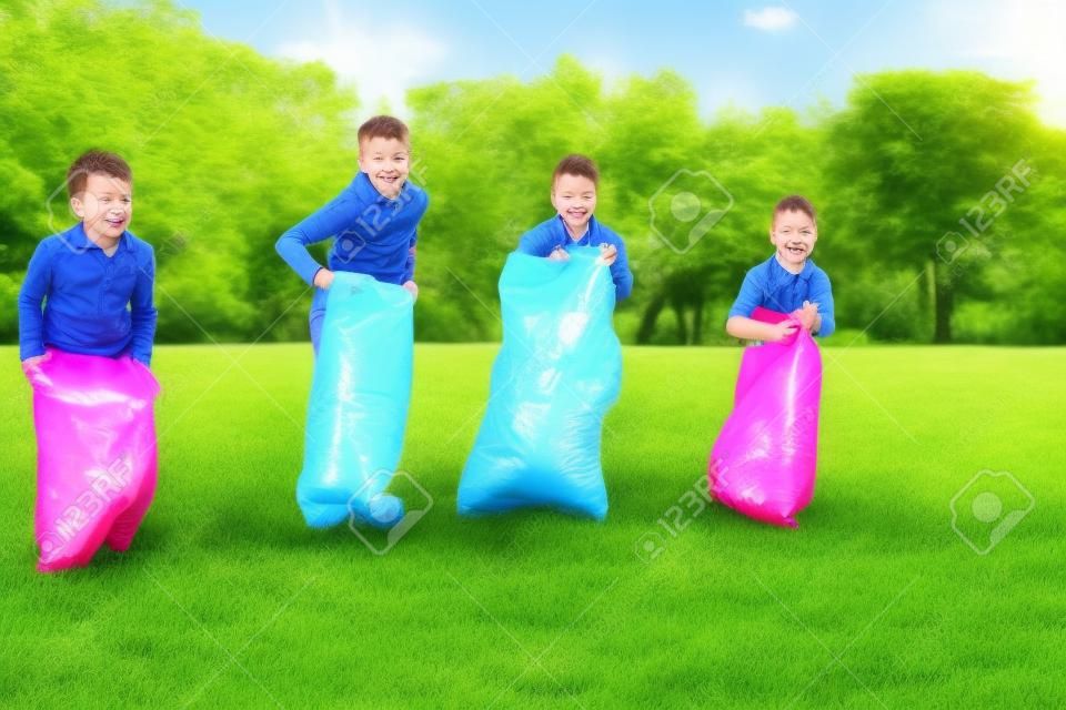 crianças felizes que jogam o jogo do salto do saco no parque
