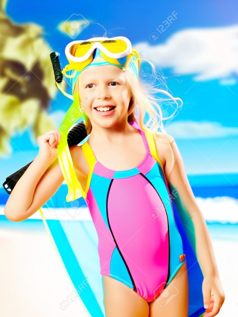 Retrato de la niña feliz disfrutando en la playa. Chica en traje de baño escolar se encuentra de color brillante con la máscara de natación en la cabeza.