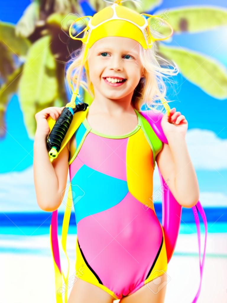 Retrato de la niña feliz disfrutando en la playa. Chica en traje de baño escolar se encuentra de color brillante con la máscara de natación en la cabeza.