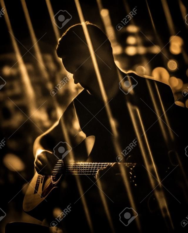 Guitarrista tocando violão. Desempenho desconectado no escuro. Técnica de dupla exposição usada.