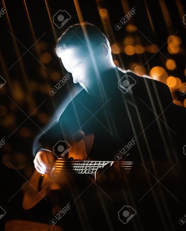 Gitarrist spielt akustische Gitarre. Steckt Leistung im Dunkeln. Gebrauchte Doppelbelichtungstechnik.