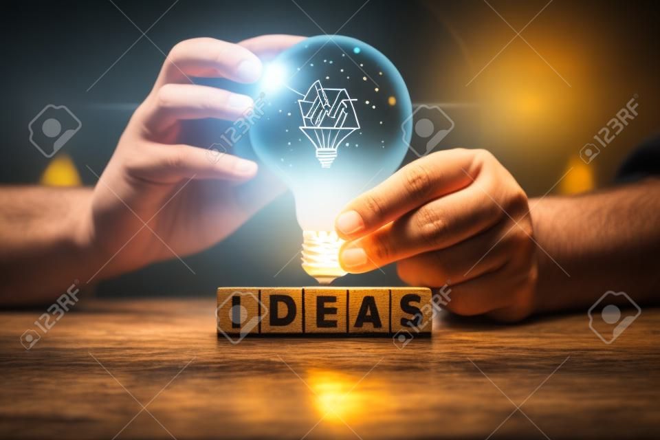 Mão segurando lâmpada no bloco de madeira com a palavra IDEAS, O conceito de nova ideia com inovação e inspiração, inovação e criatividade