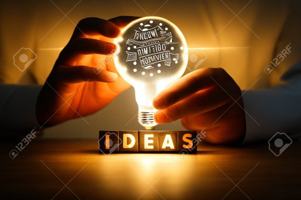 Mão segurando lâmpada no bloco de madeira com a palavra IDEAS, O conceito de nova ideia com inovação e inspiração, inovação e criatividade